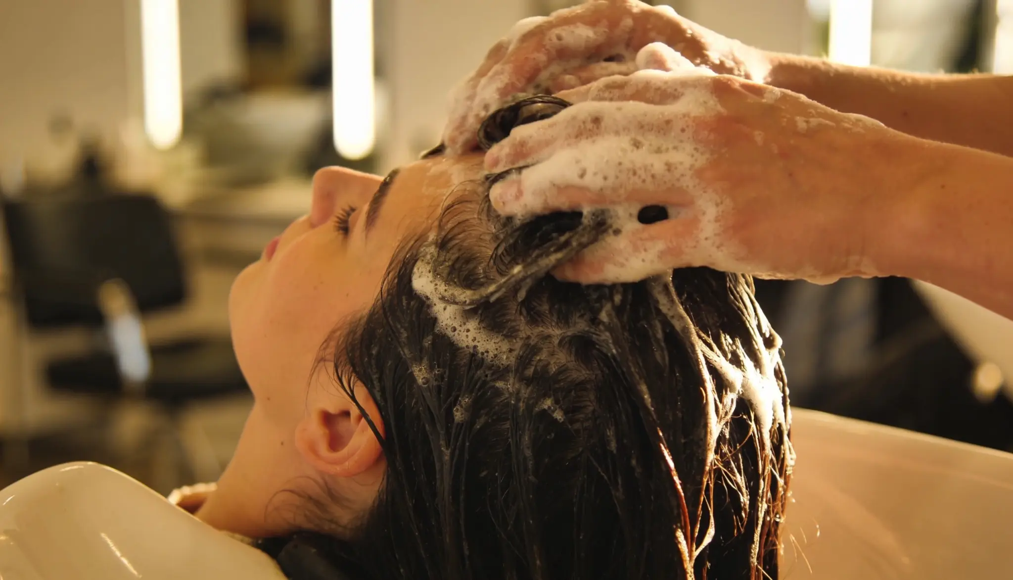 person receiving a gentle scalp massage during hair washing to promote healthy thicker looking hair