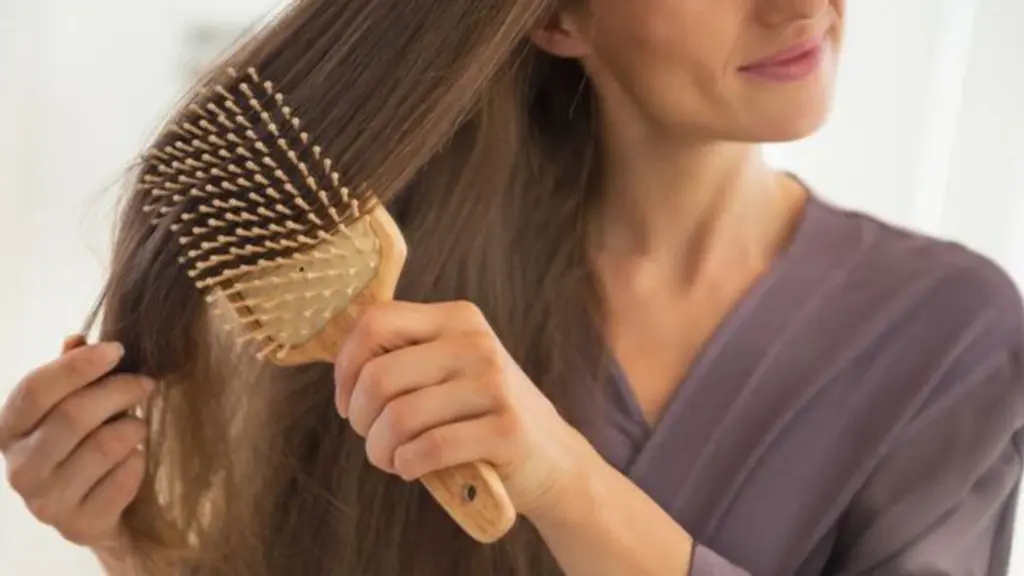 Woman in a purple top brushes her long brown hair with a wooden paddle brush.