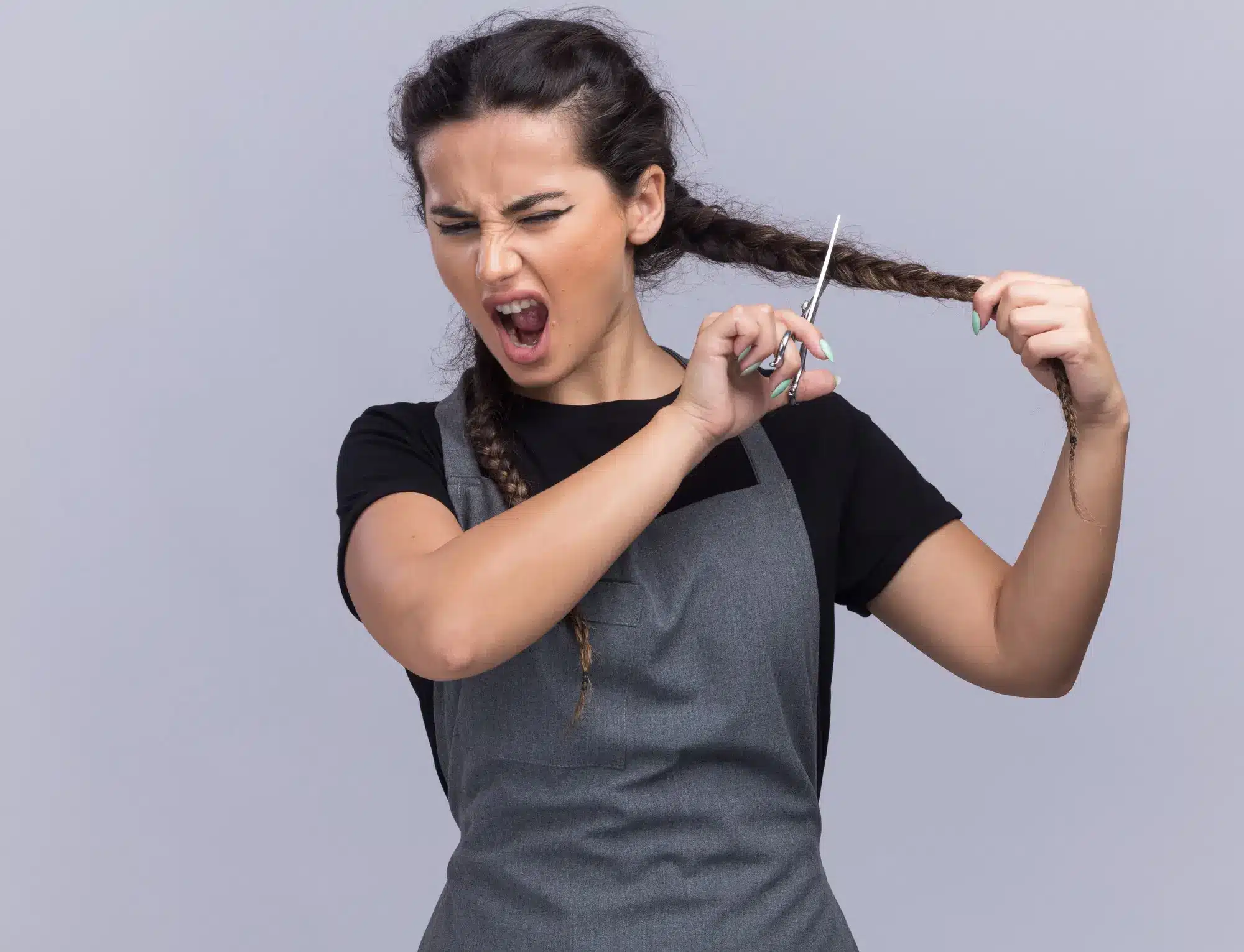 Woman in gray apron cutting her braided hair with scissors against plain background