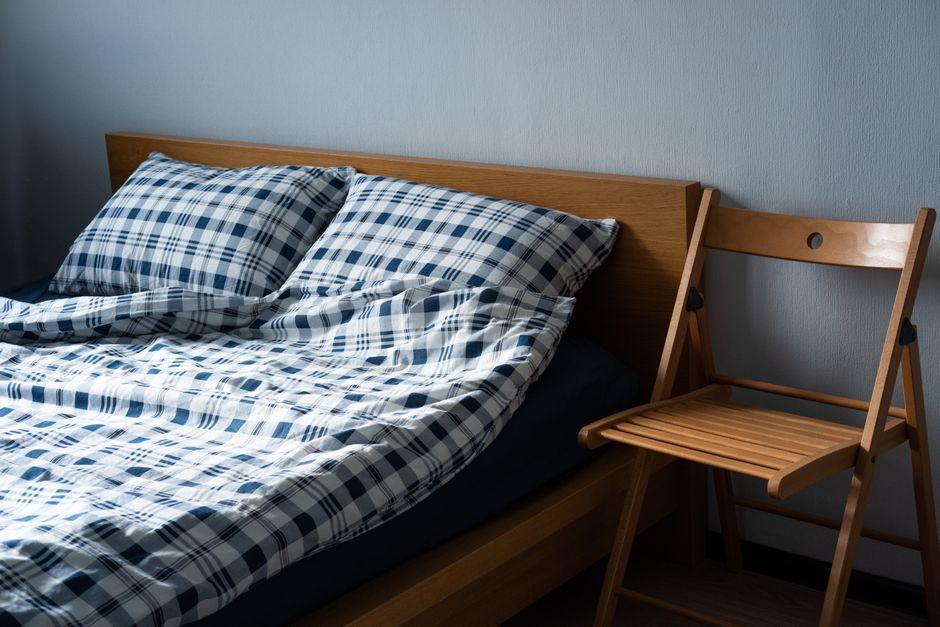 Plaid blue and white bedding on wooden bed next to wooden folding chair